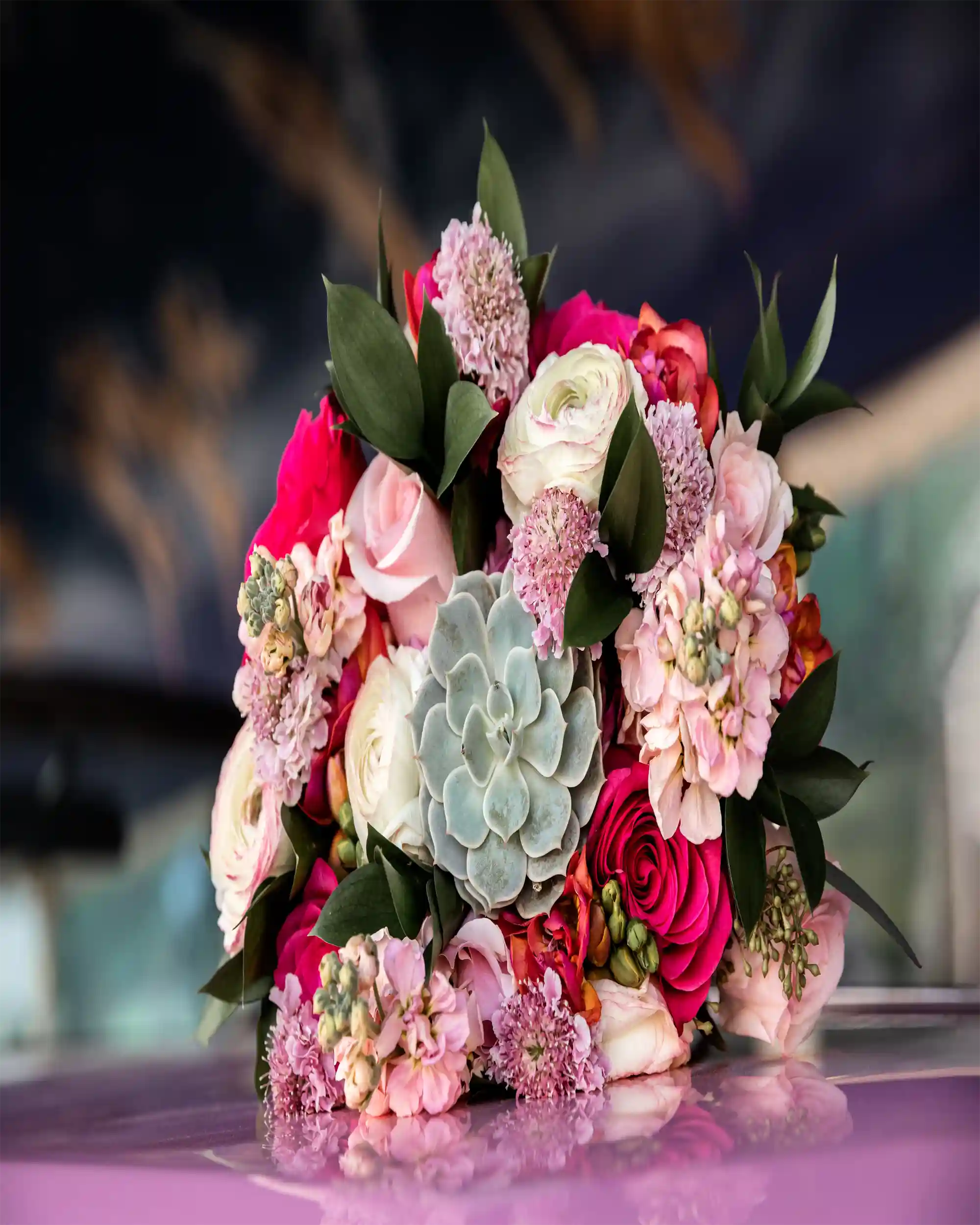 Colorful floral arrangement with pink, red, and green flowers on a reflective surface.