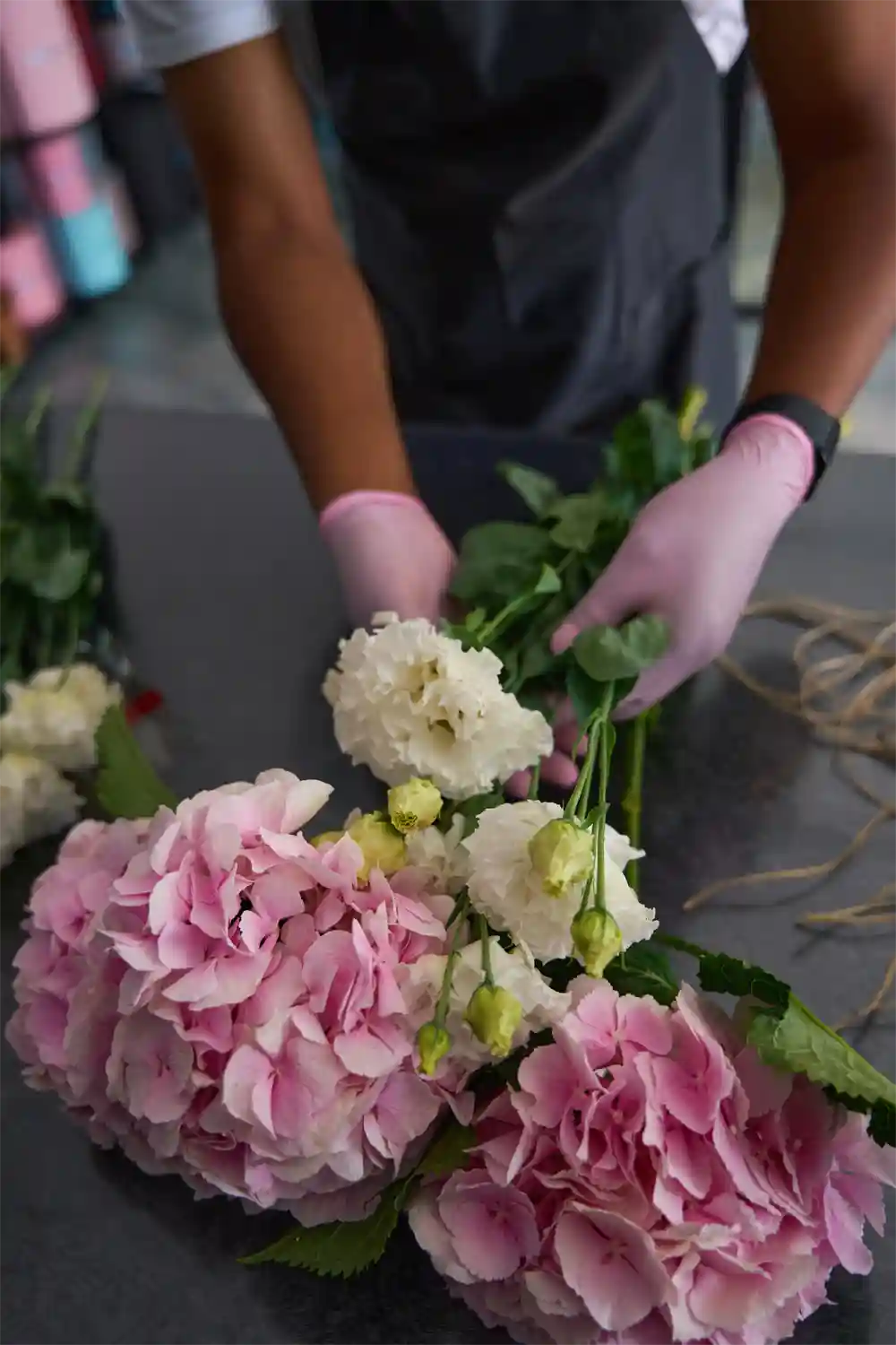 Person arranging flowers with pink gloves on a table.