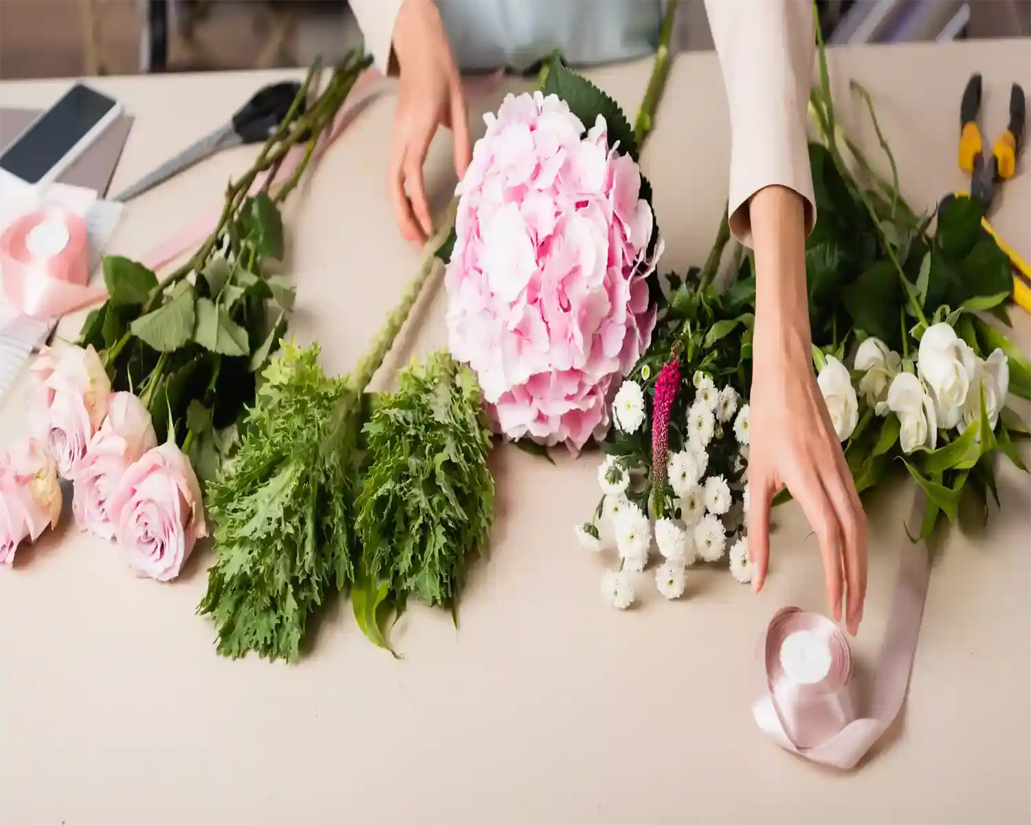 Person arranging flowers on a table with tools and a phone in the background
