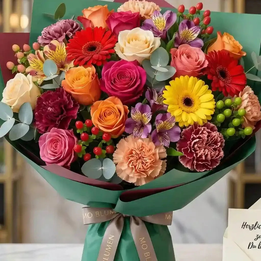 Farbenprächtiger Blumenstrauß von MO BLUMEN mit Rosen, Gerbera und Nelken in verschiedenen leuchtenden Tönen, in grünes Papier gewickelt und mit MO BLUMEN Markenband.