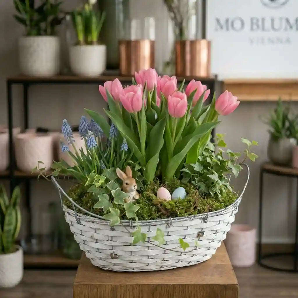 Modernes Frühlingsgefäß mit rosa Tulpen von MO BLUMEN in weißem, geflochtenen Korb mit Muscari, Efeu, Osterhase und Eiern.