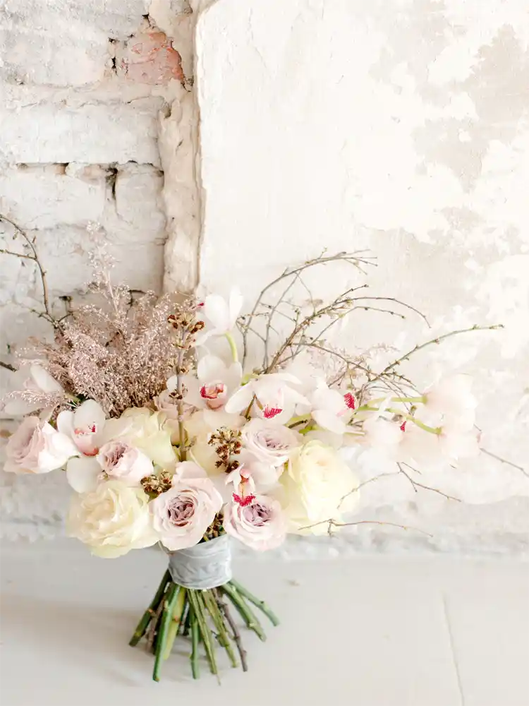 Bouquet of flowers with pink and white tones against a textured white wall.