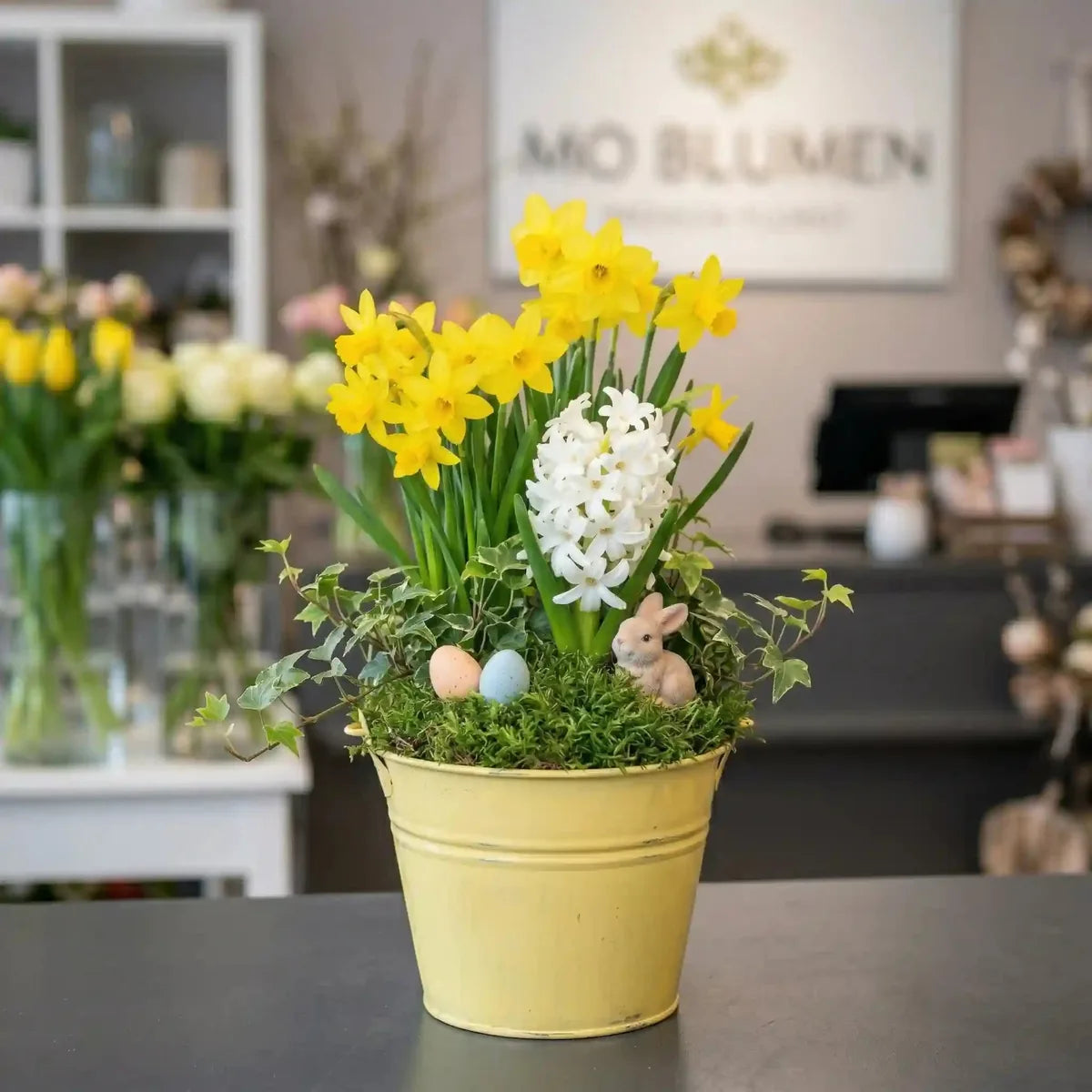Gelber Pflanzkorb mit weißen Hyazinthen und gelben Narzissen von MO BLUMEN, dekoriert mit Moos, Eiern und einem Hasen.