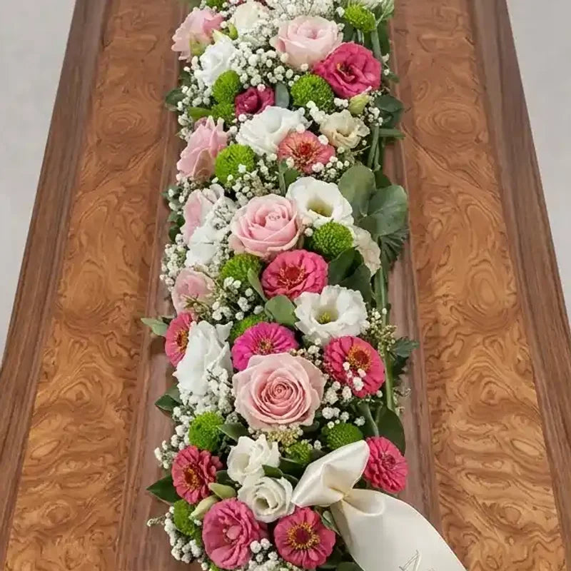 Rosafarbener Sargschmuck mit Lisianthus von MO BLUMEN, dekoriert mit Rosen, weißen Blüten und einem weißen Band auf Holzuntergrund.