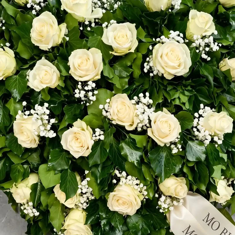 Biedermeier Trauergesteck mit weißen Rosen von MO BLUMEN, umrandet von grünem Efeu und Schleierkraut, mit hellem Schriftband.