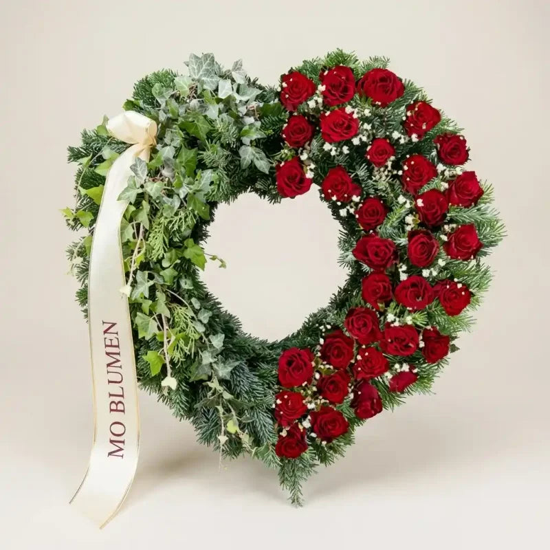 Trauerherz aus Efeu und roten Rosen von MO BLUMEN, verziert mit Schleierkraut und einem weißen Schleifenband.