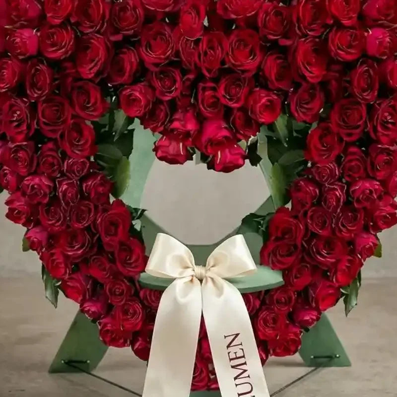 Stehendes Trauerherz aus roten Rosen von MO BLUMEN, auf einem grünen Ständer, verziert mit einem cremefarbenen Band mit Schriftzug.