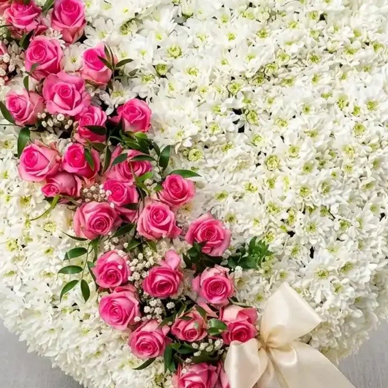 Weißes Trauerherz mit rosa Rosen Kaskade von MO BLUMEN, geformt aus weißen Blüten und cremefarbenem Band.