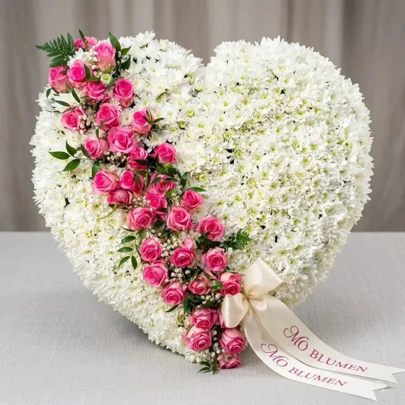Weißes Trauerherz aus Chrysanthemen mit rosa Rosenkaskade von MO BLUMEN, verziert mit grünen Blättern und einem beschrifteten Band.