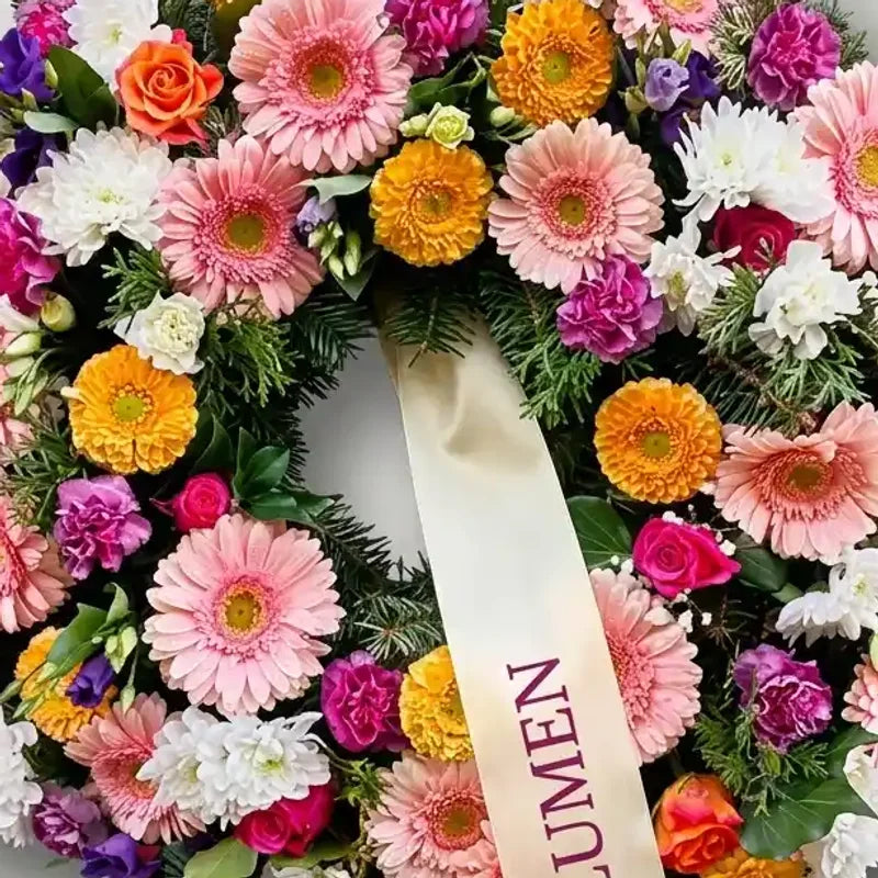 Bunter Trauerkranz von MO BLUMEN mit Gerbera, Rosen und weiteren Blüten in leuchtenden Farben und hellem Satinband mit Schriftzug.