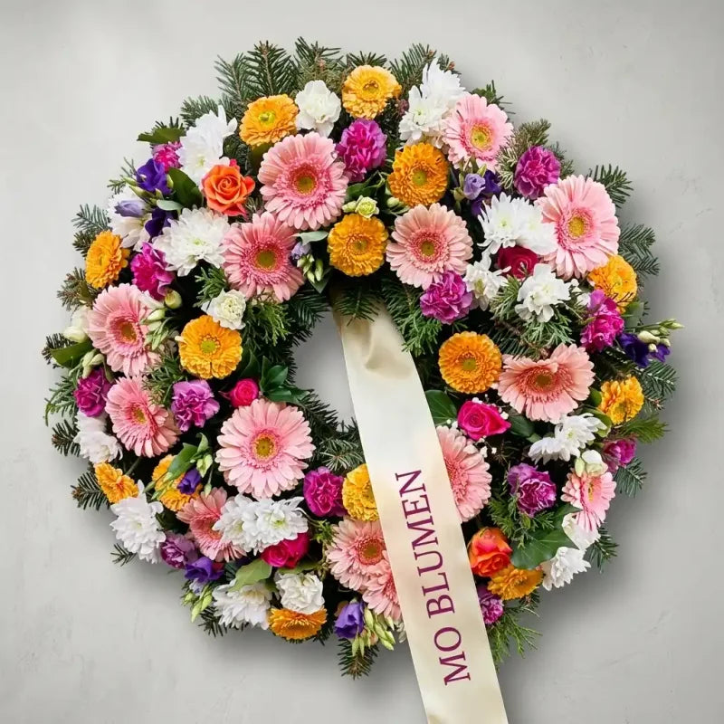 Bunter Trauerkranz von MO BLUMEN mit farbenfrohen Blumen und einem cremefarbenen Band.