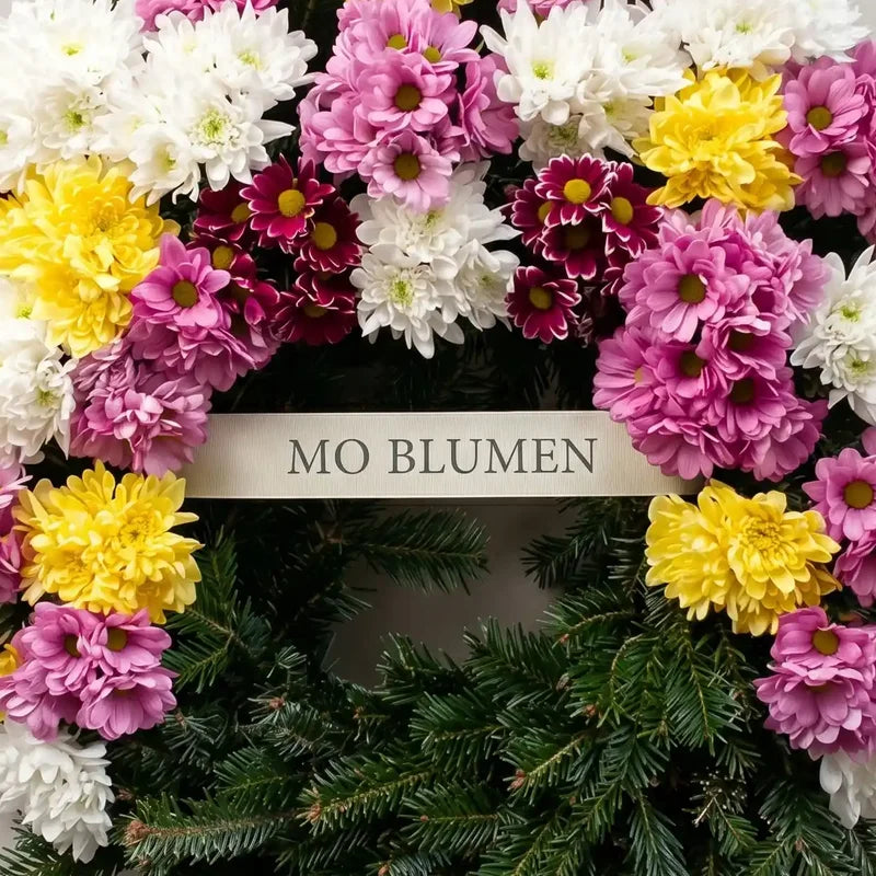 Bunter Trauerkranz aus Chrysanthemen von MO BLUMEN in Weiß, Gelb, Rosa und Weinrot, mit Tannengrün und beschriftetem Band.