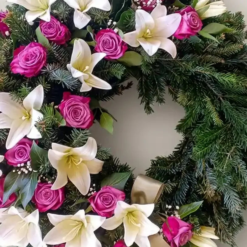 Trauerkranz mit weißen Lilien und rosa Rosen von MO BLUMEN, aus grünen Tannenzweigen mit goldener Schleife.