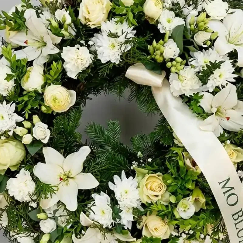 Weißer Trauerkranz von MO BLUMEN mit opulenten weißen Blumen, grünem Laub und cremefarbenem Band.