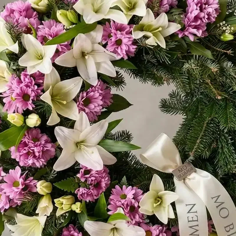 Rosa-weißer Trauerkranz von MO BLUMEN mit weißen Lilien, rosa Chrysanthemen und einem weißen Band mit Text.