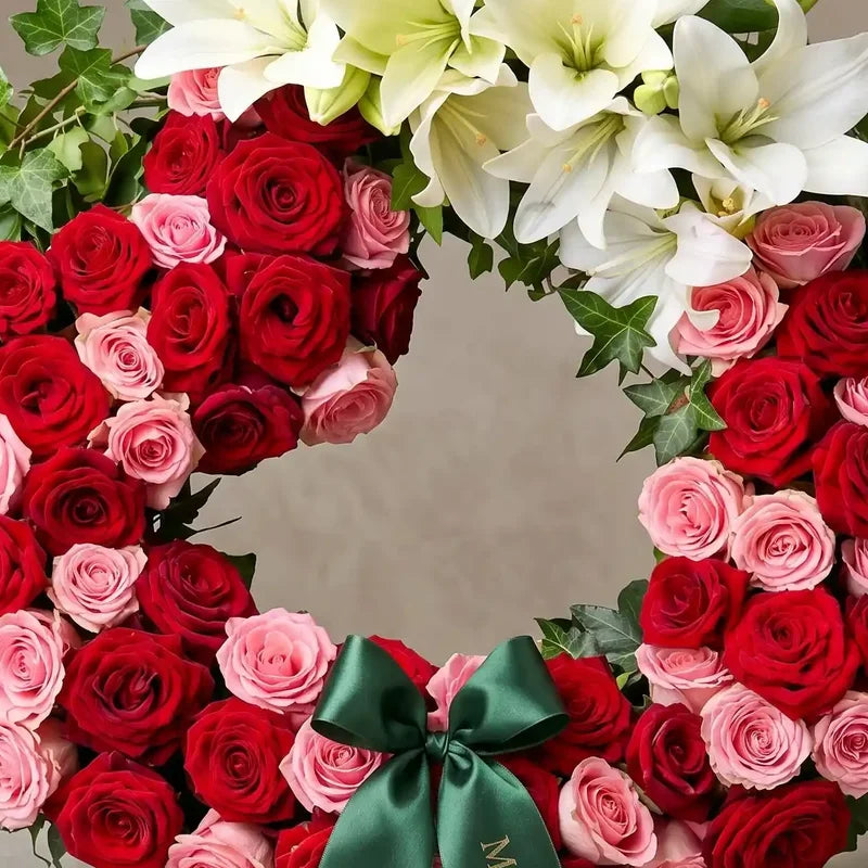 Trauerkranz aus rot-rosa Rosen und Lilien von MO BLUMEN, geschmückt mit Efeu und einer dunkelgrünen Satinschleife.
