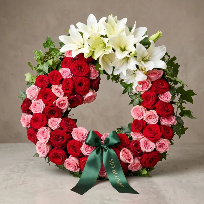 Rot-rosa Trauerkranz mit weißen Lilien von MO BLUMEN, mit grüner Schleife und Efeu.