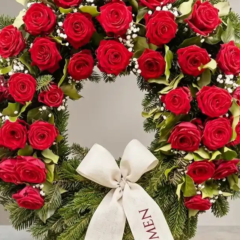Trauerkranz mit roten Rosen von MO BLUMEN, aus Tannengrün mit weißen Schleierkrautblüten und heller Schleife mit Schriftzug.