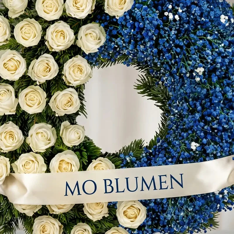 Trauerkranz in Weiß-Blau Kontrast von MO BLUMEN mit weißen Rosen, blauem Schleierkraut und einem weißen Band.