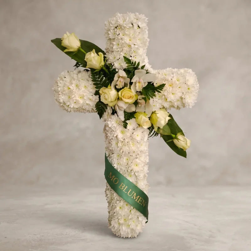 Weißes Trauerkreuz von MO BLUMEN, verziert mit weißen Orchideen, gelben Rosen und einem grünen Band.